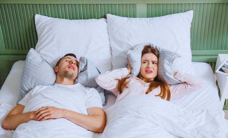 ragazza si copre le orecchie con il cuscino mentre un uomo russa